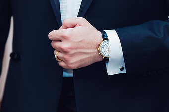 The hand of a man in a suit with a watch on.